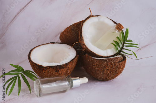 close up selective focus glass bottles with coconut oil on a blurred background of cracked coconuts and palm leaves