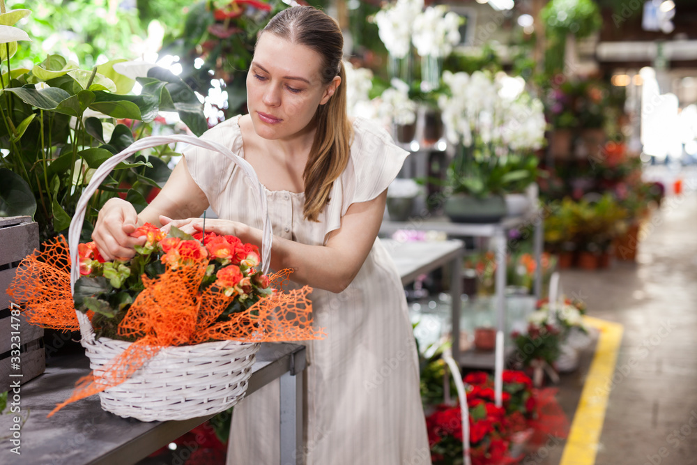 Cheerful smiling woman holding basket with red roses in floral shop