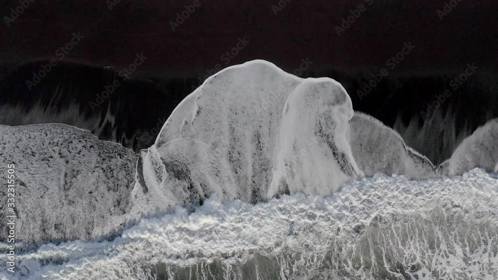 Aerial straight down on Atlantic ocean waves breaking on black sand beach in south Iceland.