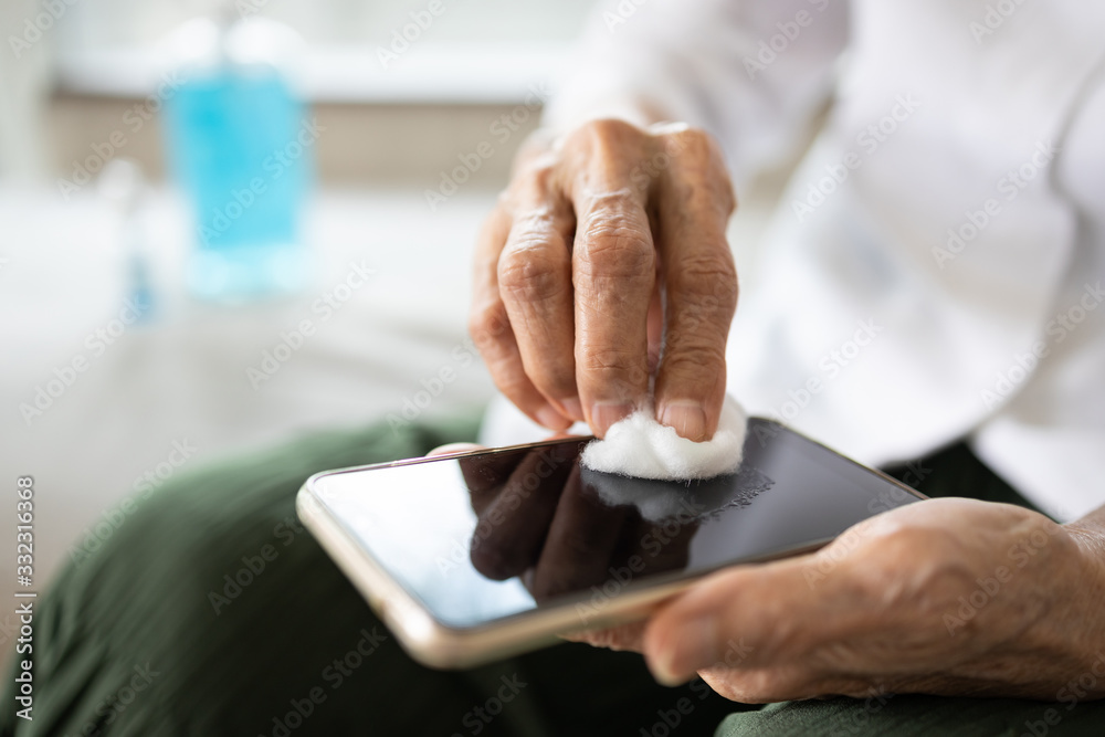 Obraz premium Hands of elderly people using cotton wool with alcohol to wipe on mobile phone to avoid contamination of Coronavirus,prevent contagious disease of Covid-19 virus,cleaning phone to eliminate of germs