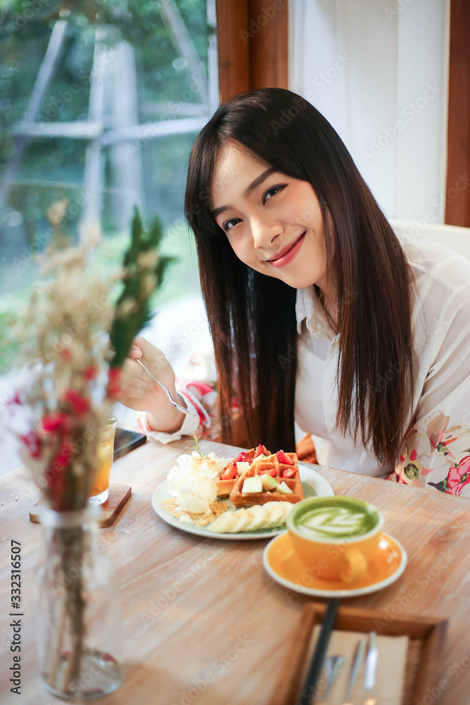 Beautiful asian woman eating delicious  waffles in coffee shop cafe.