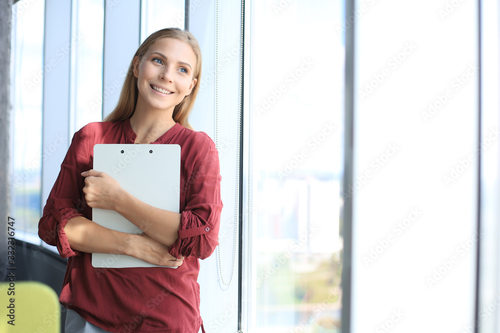 Attractive business woman looking at camera and smiling while standing in the office Attractive business woman looking at camera and smiling while standing in the office