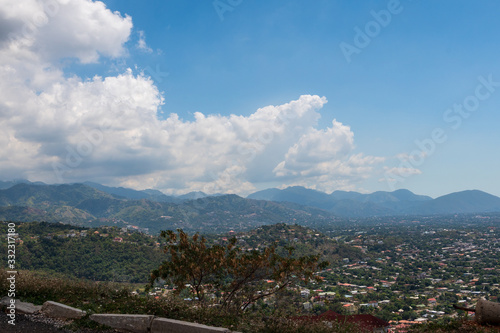 a blue sky filled with white clouds hovers over a tranquil scene of a mountain range backing a town in a valley