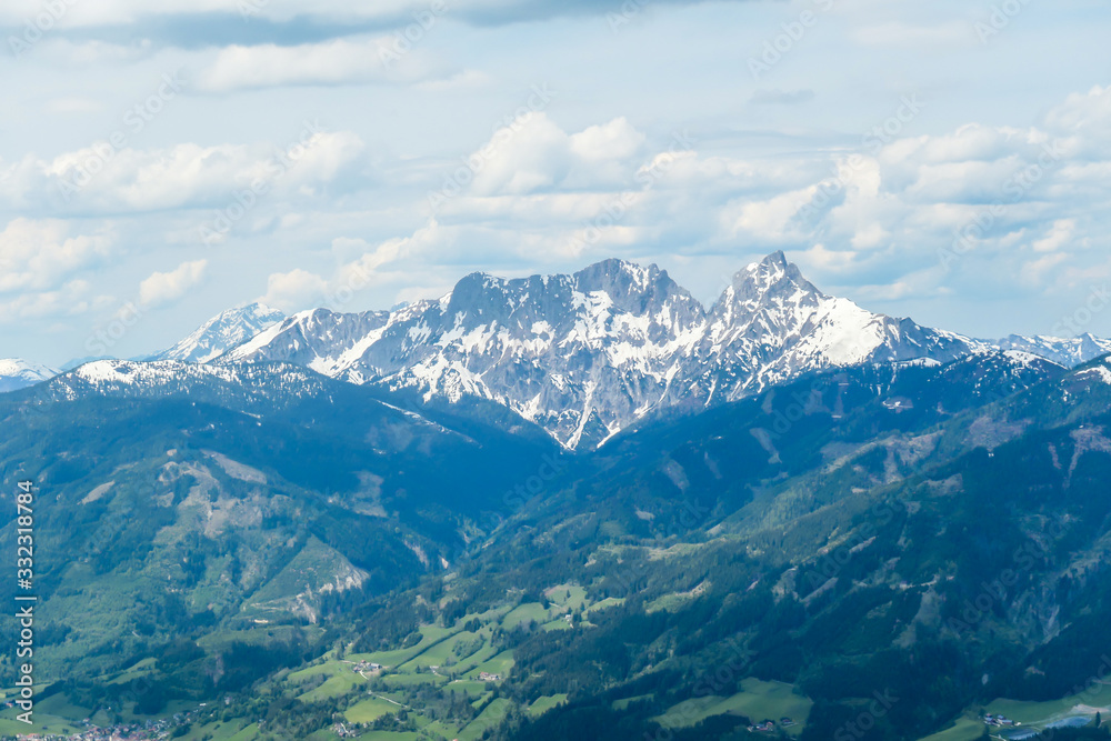 A distant view on the snowy slopes of Austrian Alps. There is a massive mountain chain in the back, partially covered with snow. Early spring coming to the Alps. Overcast. Achievement and fun.