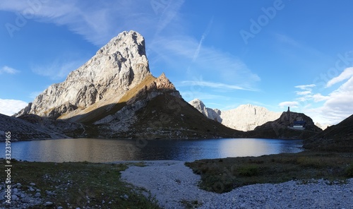 Panoramic shot of a soft reflection of an Alpine mountain in Wolayer Lake Austria. Completely still surface of the lake. Mountain is catching the first sunbeams. Peace of mind, calmness. High altitude