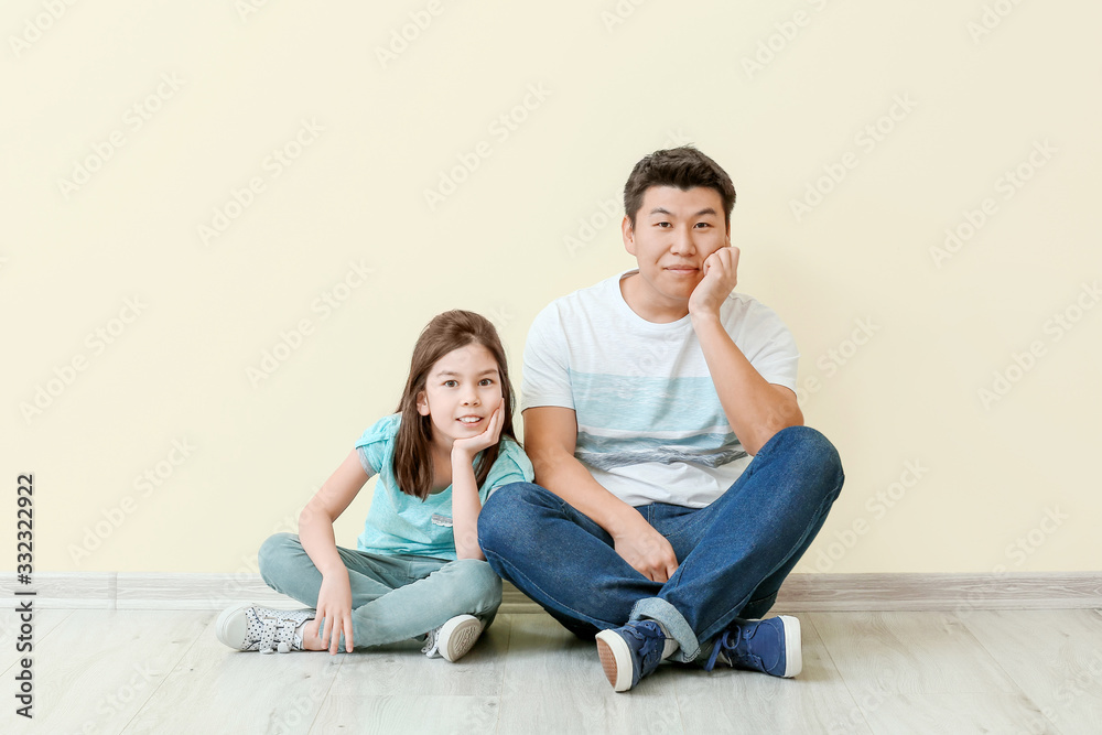 Happy Asian man and his little daughter sitting near color wall Happy Asian man and his little daughter sitting near color wall