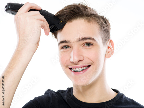 Smiling Teenage boy cuts his own hair with an electric razor. Happy Young man cuts his hair with a razor