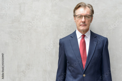 Handsome mature businessman in suit with eyeglasses against concrete wall