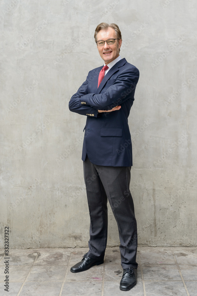 Full body shot of happy handsome mature businessman smiling with arms crossed outdoors Full body shot of happy handsome mature businessman smiling with arms crossed outdoors