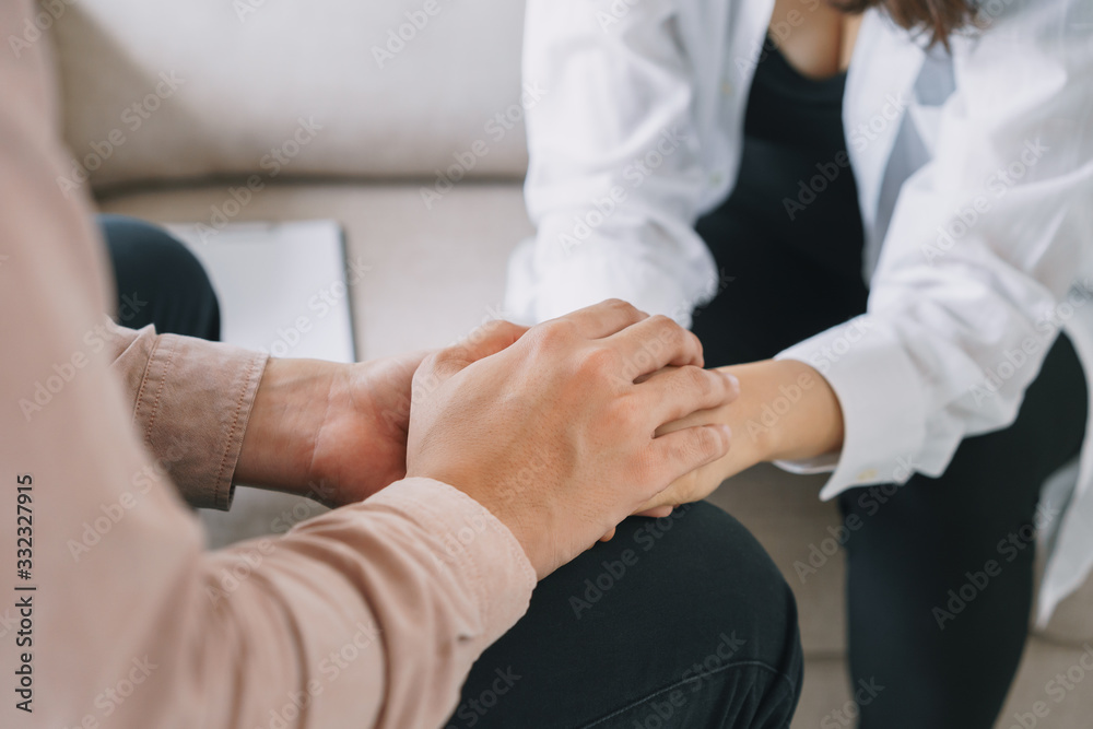 Close-up of psychiatrist hands together holding palm of her patient.  Psychological male comforting and holding a woman hand while sitting on the sofa. psychologist concept