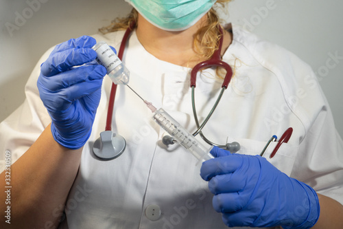 Nurse introducing the coronavirus vaccine into a syringe.  The syringe has the 2019-NcOv vaccine.  the nurse wears blue gloves and a mask.