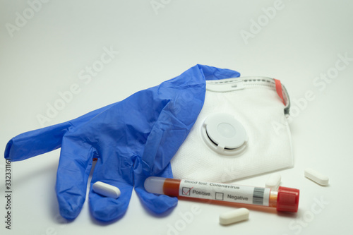 Blood test of the coronavirus surrounded by pills, mask and gloves. The blood tube is labeled positive for 2019-NcOv.