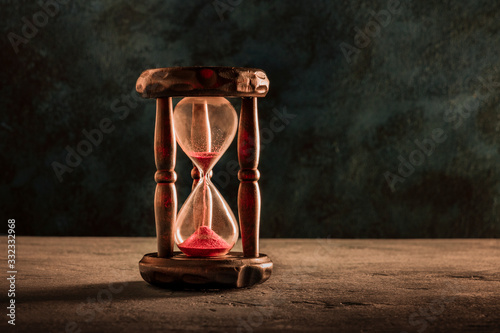 Time is running out concept. An hourglass with sand falling through, on a dark background with a place for text, toned image