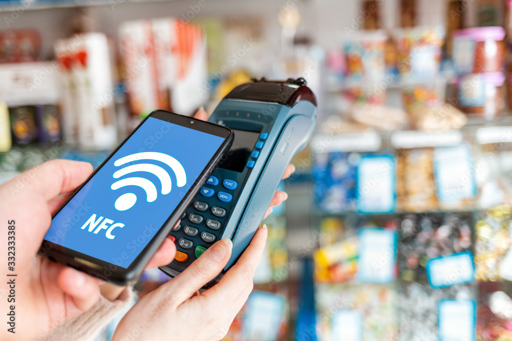 Women's hands are held by a payment terminal and a man pays for a purchase using a smartphone.On the phone screen, the wi-fi network. The concept of NFC, business and banking transactions