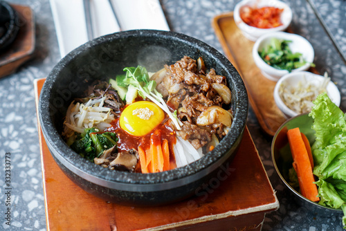 Bibimbap with pork and egg yolk. A bowl of rice topped with many vegetable, fried pork and egg yolk, a famous traditional Korean food called "Bibimbap", served with side dish.