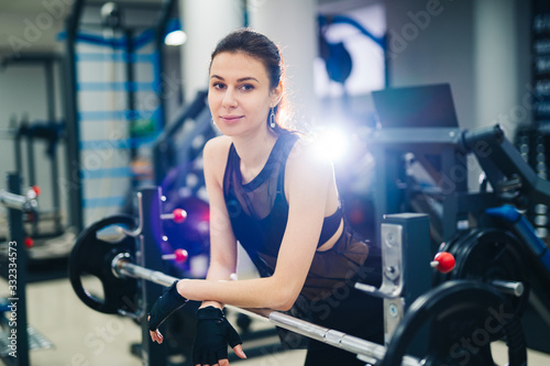 Portrait of beautiful fit woman resting after lifting barbell in fitness centre. Young sports muscular female taking break between repetitions. Closeup. Healthy life concept.