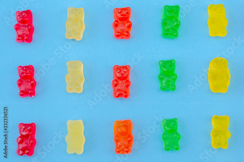 Delicious bright colored jelly bears on a blue background laid out in the same order, top view