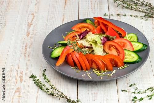 tomato, bell pepper, cucumber slices, lettuce and thyme on gray plate, served on white wooden background in rustic style with copy space, sliced raw assorted vegetables in national food restaurant