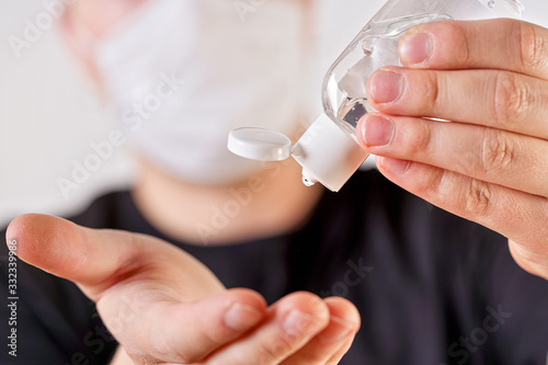 Detail on young man hands holding antibacterial gel about to drop and clean, blurred face with mouth nose mask in background. Can be used as coronavirus or covid19 outbreak prevention illustration