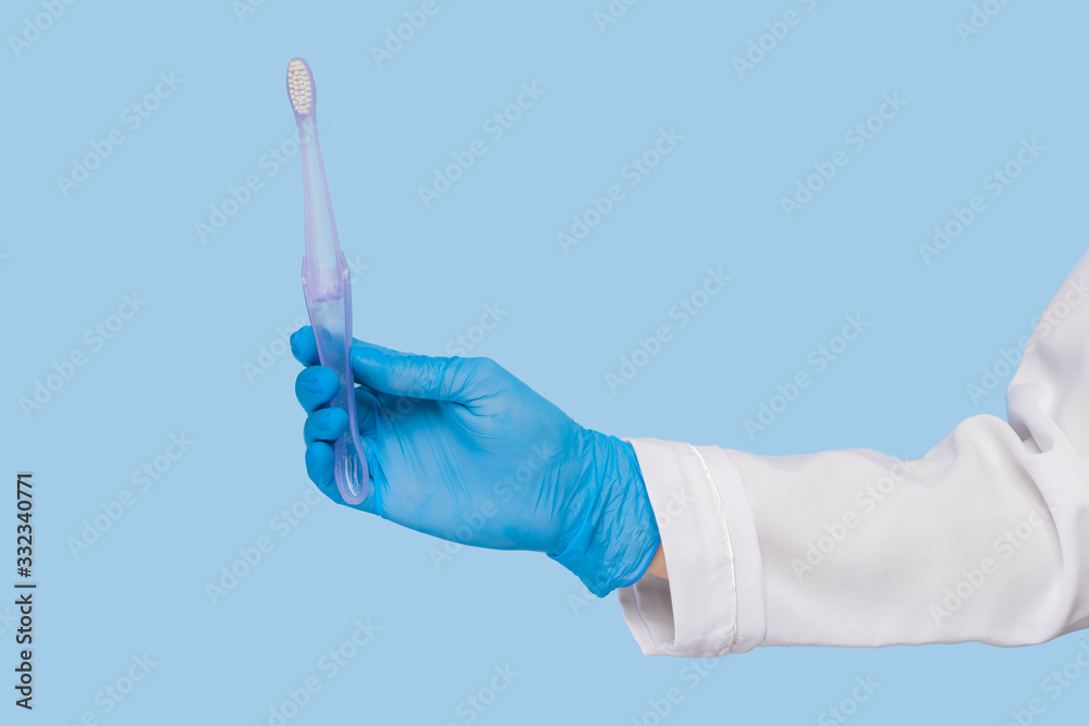 Doctor's hands in sterile gloves hold a new toothbrush on a blue background. Oral hygiene concept. dentistry