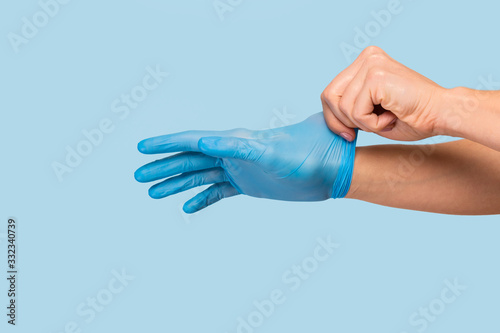 The doctor puts on sterile gloves on a blue background. Infection control concept. Danger of spread of infection