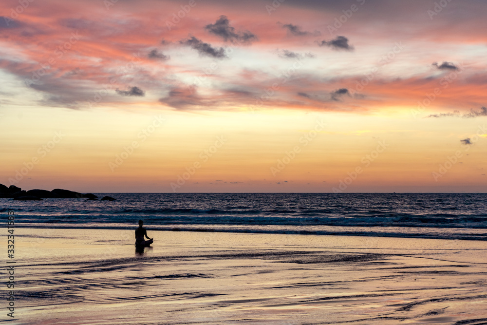 young unrecognizable woman meditating at agonda beach at sunset in goa, india