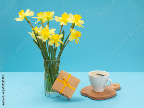 Bouquet of yellow daffodils in vase with gift box on a blue background.