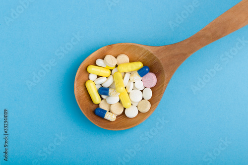 pharmaceutical medicine pills, tablets and capsules on wooden spoon, close up. Blue medical background . Wooden spoon with pills or capsules.