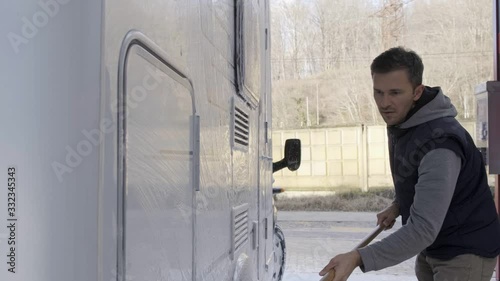 A young man of European nationality washes a car at a car wash. Self catering. Seasonal RV Recreational Vehicle Motorhome Cleaning Using Pressure Washer. RV Camper. Caucasian Men