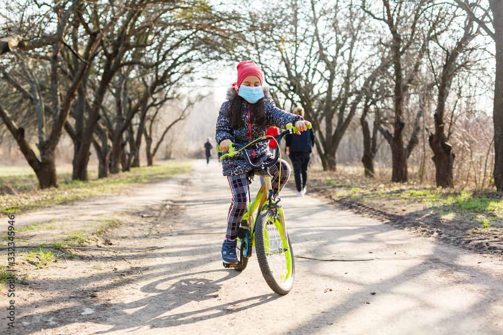 Fototapeta premium Little girl wearing medical mask prevent flu, pollutions and covid-19 riding bicycle outdoor.