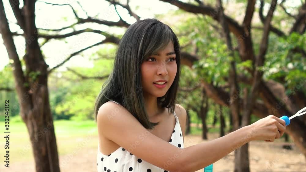 South East Asian ethnic 20s woman blowing air bubbles in the park Young Happy girl wears stylish dress with trees in background. Outdoor summer weekend activity South East Asian ethnic 20s woman blowing air bubbles in the park Young Happy girl wears stylish dress with trees in background. Outdoor summer weekend activity