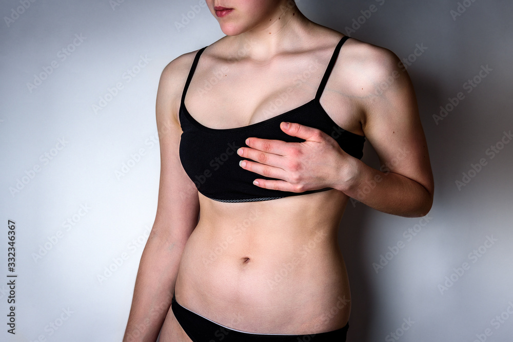 Young woman with breast pain on gray background.