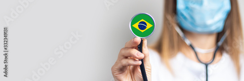 female doctor in a medical mask holds a stethoscope on a light background. Added flag of Brazil. Concept medicine, level of medicine, virus, epidemic. Baner photo