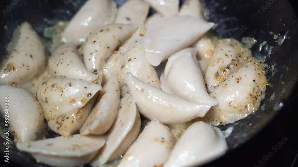 Pierogis added to frying pan with red tongs in super slow motion. Cooking pirogies coated in oil and herbs in a black frying pan.