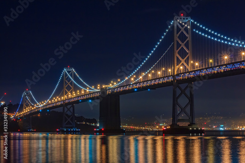 San Francisco Bay Bridge at night, lit up by yellow and blue lights, reflecting of the water in the Bay, long exposure © SvetlanaSF