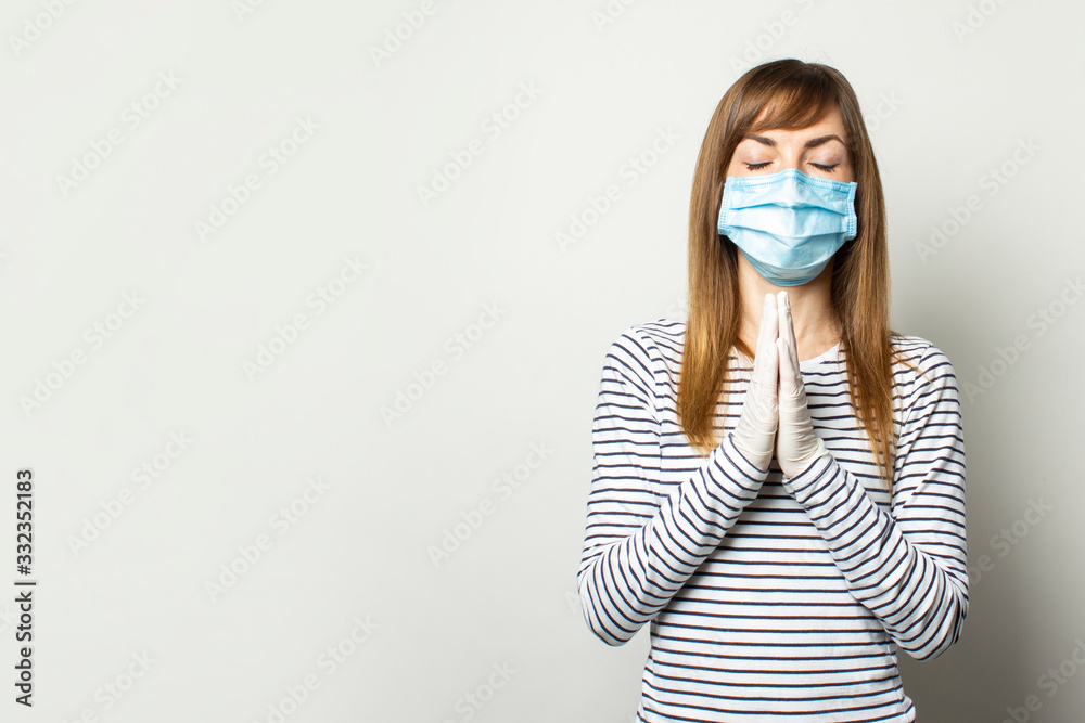 Young woman in protective medical mask and latex gloves holds her hands near her chest, prayer pose on a light isolated background. Concept of coronavirus, pandemic, prayer, appeal to God, religion Young woman in protective medical mask and latex gloves holds her hands near her chest, prayer pose on a light isolated background. Concept of coronavirus, pandemic, prayer, appeal to God, religion