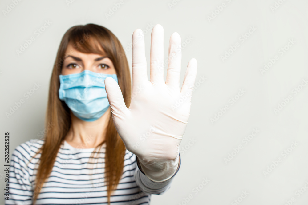 Young woman in a protective medical mask and latex gloves holds her hand and shows the viewer on a light isolated background. Concept of coronavirus, clean hands, no virus, stop. Banner. copy space - obrazy, fototapety, plakaty 