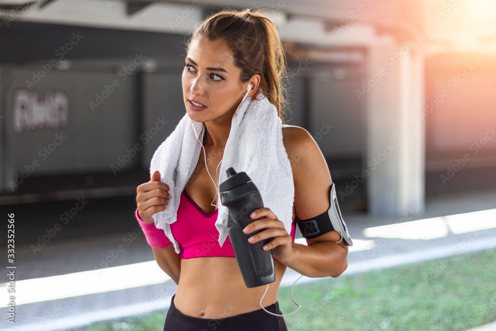 Shot of beautiful female runner standing outdoors holding water bottle and drinking. Fitness woman taking a break after running workout. Stay hydrated Shot of beautiful female runner standing outdoors holding water bottle and drinking. Fitness woman taking a break after running workout. Stay hydrated