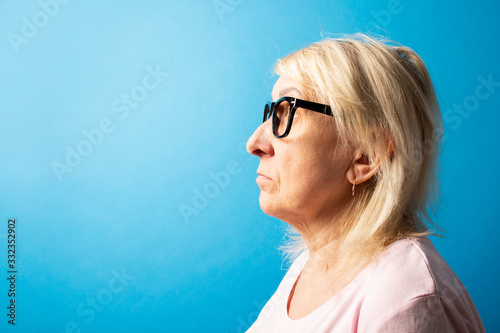 Old woman with glasses looks away on a blue isolated background. The concept of sadness, care for old people, good eyesight. Banner. copy space © Alex