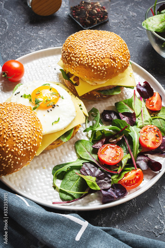 Breakfast two burgers with chicken, fried egg and cheese on a dark stone background