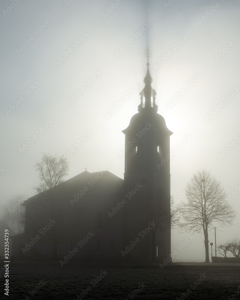 Fototapeta premium Slovenian church surrounded by fog during winter with the sun shining through