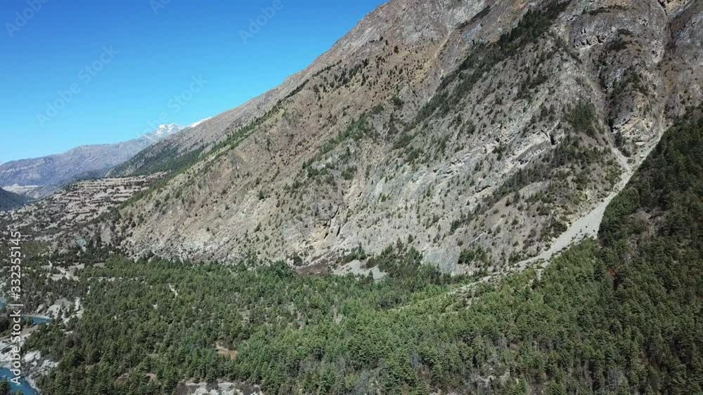 A panoramic shot of Manang Valley in Nepalese Himalayas. There is a small river in the valley. High mountains around. Dense forest at the bottom of the valley, barren slopes. Annapurna Circuit Trek A panoramic shot of Manang Valley in Nepalese Himalayas. There is a small river in the valley. High mountains around. Dense forest at the bottom of the valley, barren slopes. Annapurna Circuit Trek
