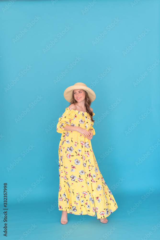 Attractive girl with brunette hair in yellow hat and dress over blue background Attractive girl with brunette hair in yellow hat and dress over blue background