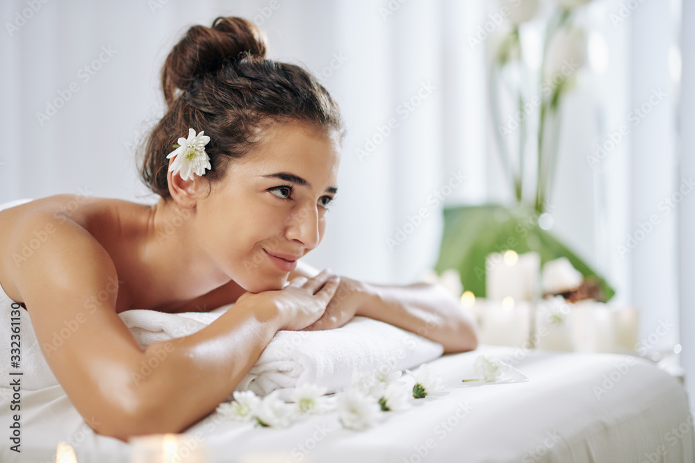 Attractive young smiling woman with flower in her hair resting in spa salon and waiting for relaxing procedure Attractive young smiling woman with flower in her hair resting in spa salon and waiting for relaxing procedure