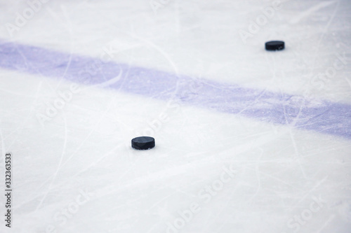Old , black ice hockey puck near blue line in ice hockey rink.