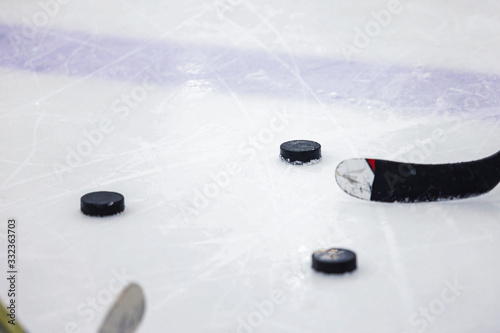 three ice hockey pucks on ice arena rink with two hockey sticks.