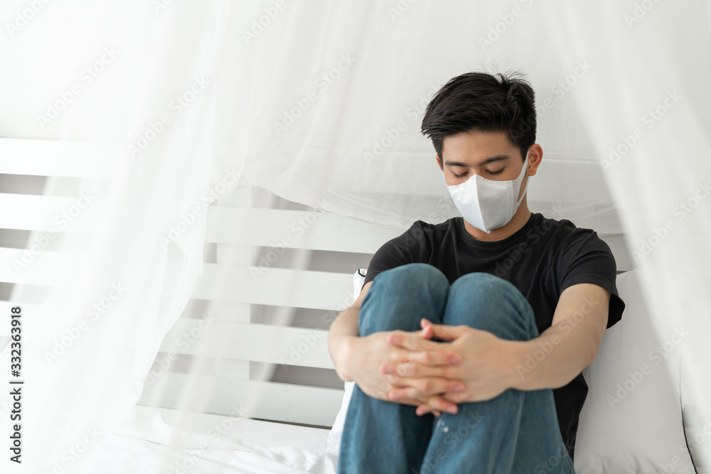 Asian man wearing Face Mask to protect feeling sick headache and cough because of Coronavirus covid-19 in quarantine room , Quarantine yourself to protect spread Covid-19 Coronavirus Asian man wearing Face Mask to protect feeling sick headache and cough because of Coronavirus covid-19 in quarantine room , Quarantine yourself to protect spread Covid-19 Coronavirus