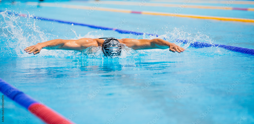Athletic man swimming in butterfly style in the swimming pool with clear blue water.