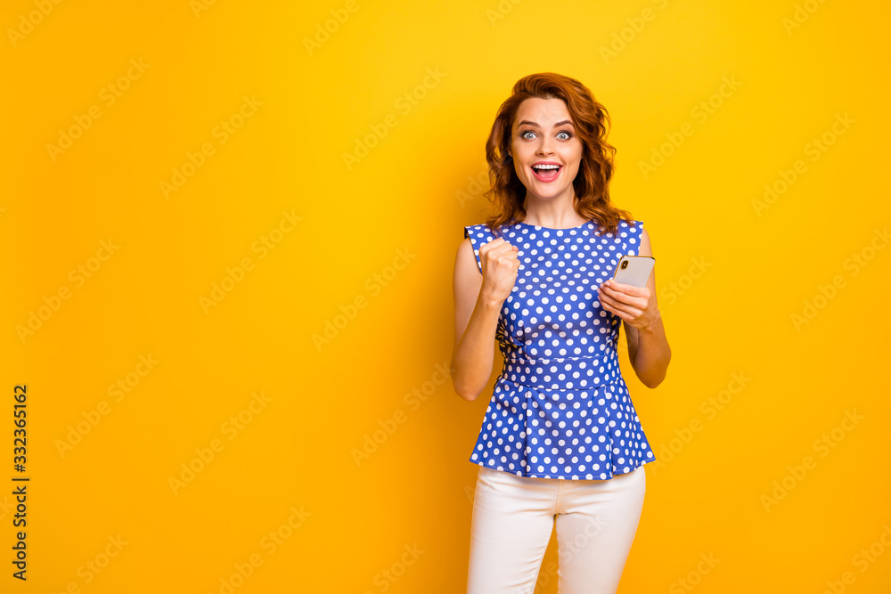 Photo of crazy funky lady blogger hold telephone hands raise fist successful influencer read comments wear polka-dot blue shirt white pants isolated yellow color background Photo of crazy funky lady blogger hold telephone hands raise fist successful influencer read comments wear polka-dot blue shirt white pants isolated yellow color background
