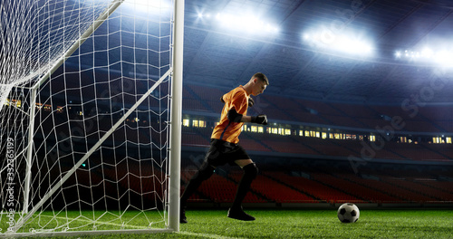 Goalkeeper kicks the ball out of the goal on the empty soccer stadium. No spectators on the tribunes. Stadium is made in 3D.